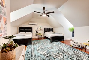 A bedroom with two beds, a ceiling fan, a large patterned rug, and a plant.