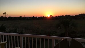 Un atardecer sobre un campo cubierto de hierba, con una barandilla blanca en primer plano.