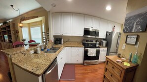 Una cocina con armarios blancos, encimera de granito, electrodomésticos de acero inoxidable y una zona de comedor de madera.