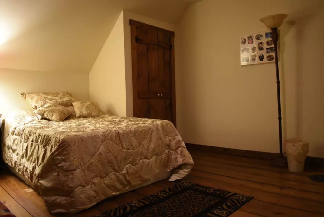 Une chambre à coucher avec un lit, une porte en bois, une lampe sur pied et un collage de photos accroché au mur.
