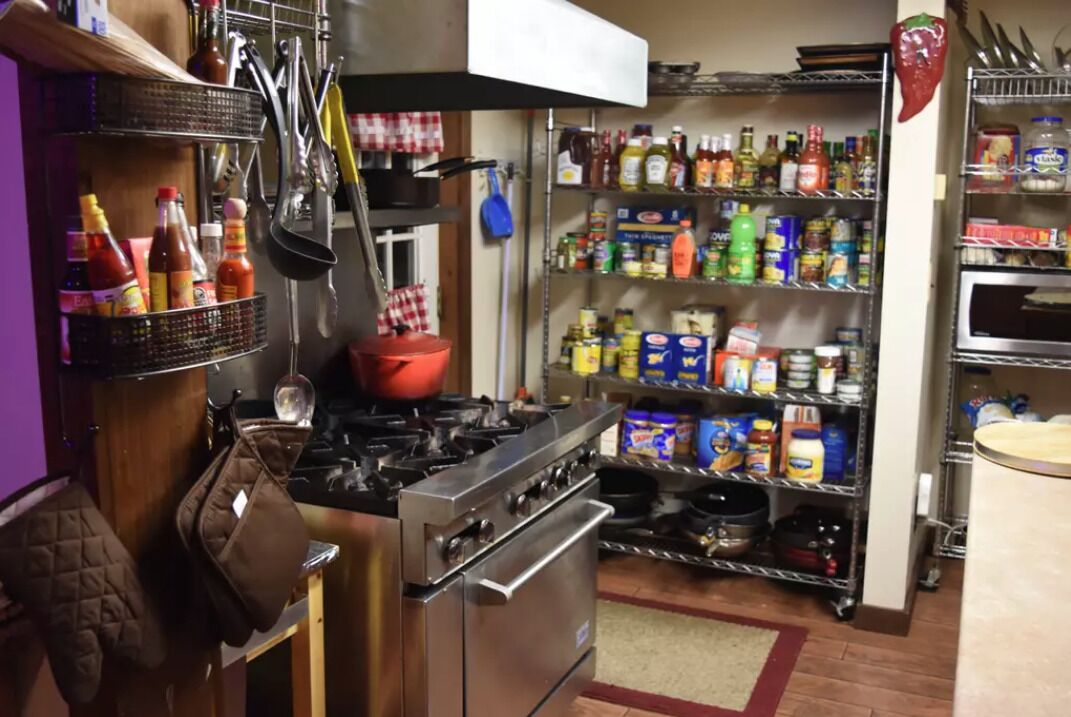 Una cocina con estufa, horno y diversos alimentos en estantes.
