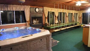 Un jacuzzi con revestimiento de piedra, una chimenea y un conjunto de columpios en una habitación con paredes de madera y alfombra verde.