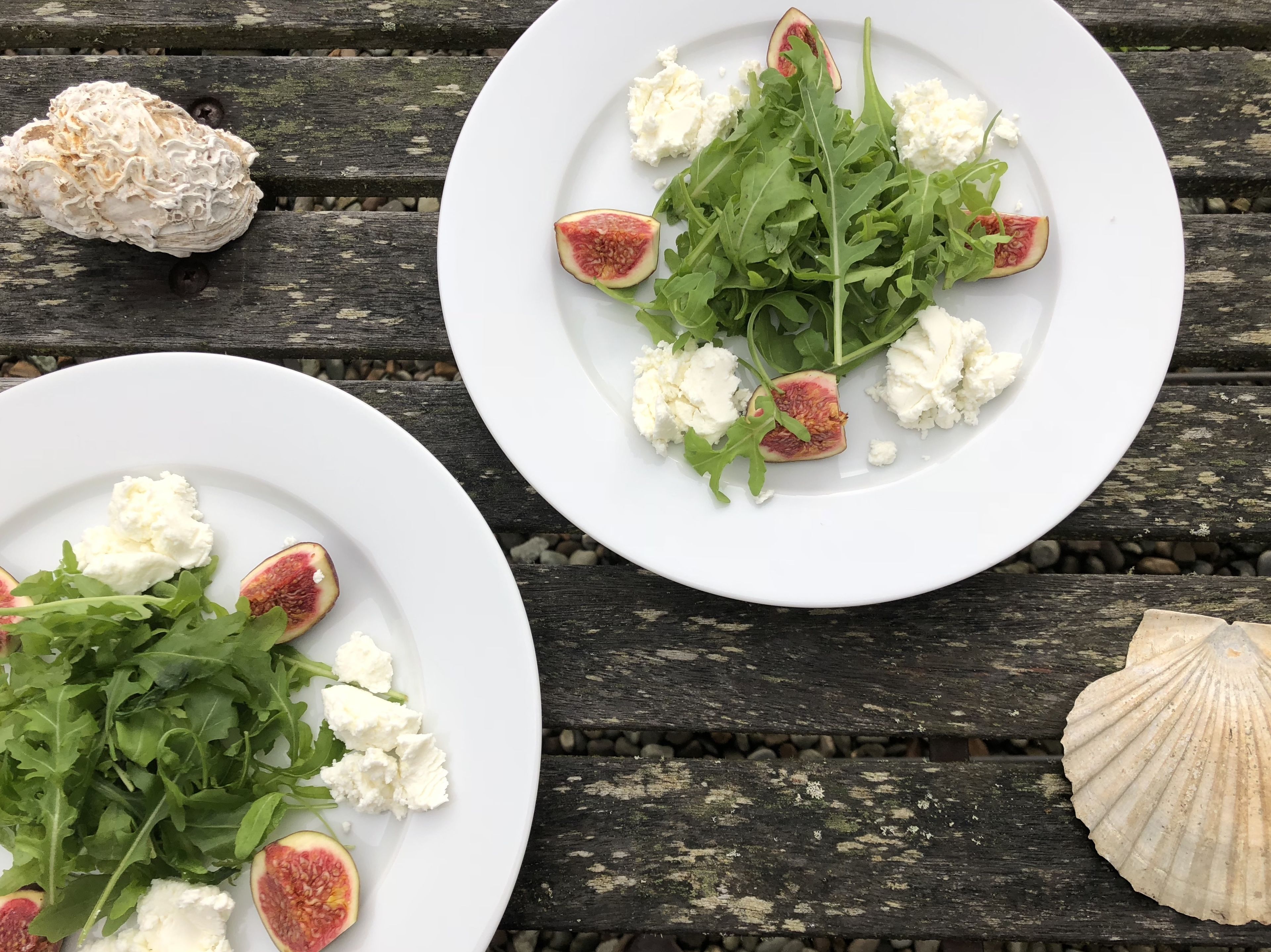 Two white plates with arugula, figs, and cheese on a wooden table.