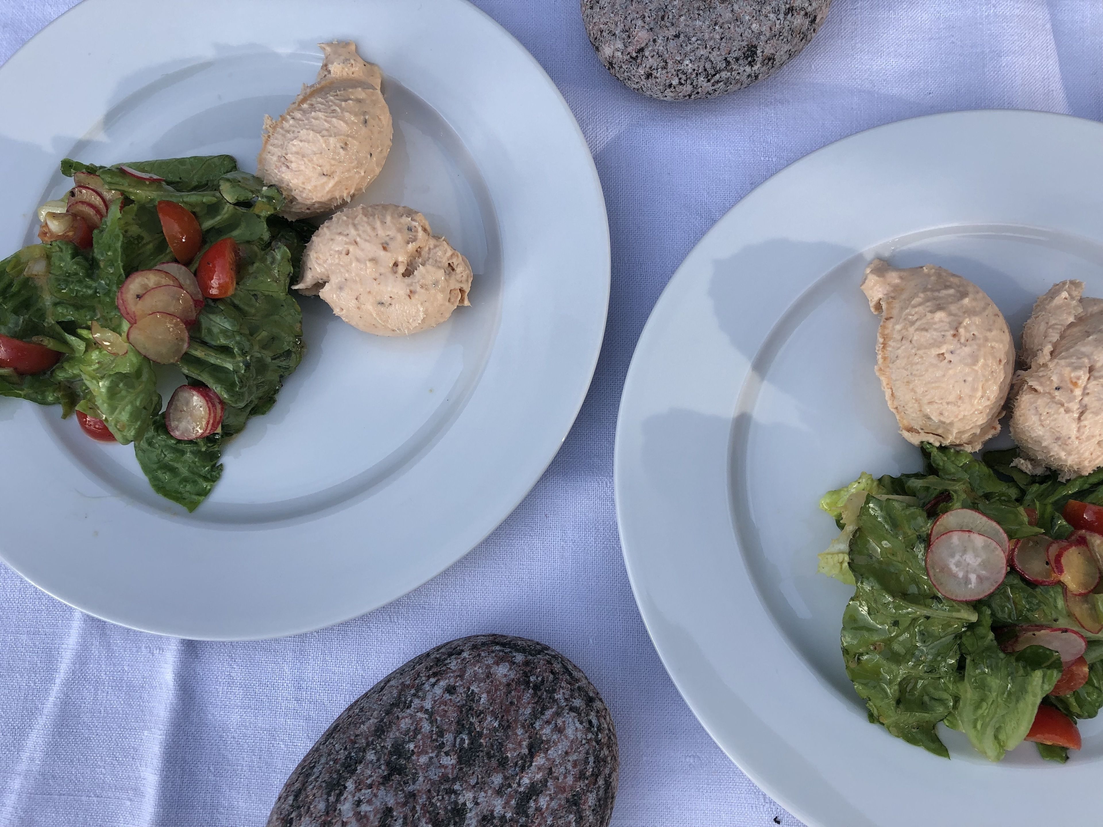 Två tallrikar med mat, bestående av sallad och kycklingbröst, placerade på ett vitt bordsduk.