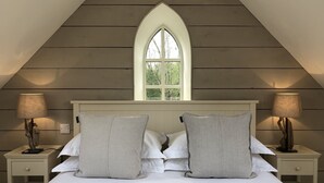 Un dormitorio con techo inclinado, una ventana, dos mesitas de noche con lámparas y una cama con almohadas.
