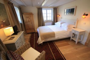 Un dormitorio con cama, mesita de noche, cómoda, silla, ventana con cortinas y lámpara.