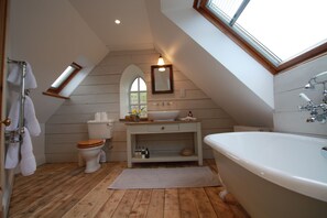 Un baño con suelo de madera, un lavabo blanco, inodoro, bañera y tragaluz.