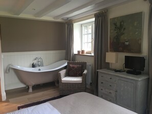 Un dormitorio con una cama grande, una bañera de estilo vintage, un sillón de mimbre, un aparador y un cuadro en la pared.