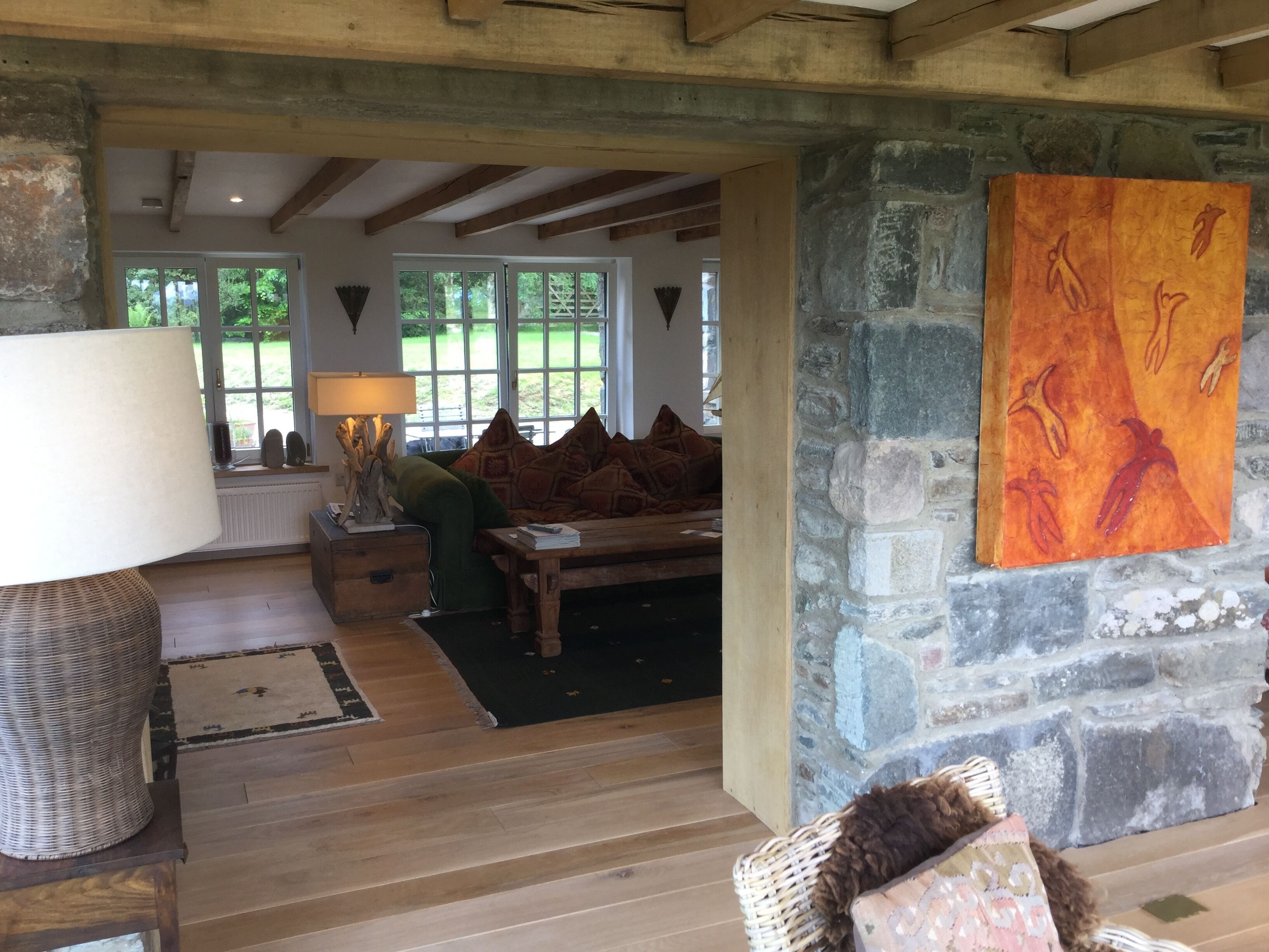 A rustic interior with a stone fireplace, wooden beams, and a large painting.