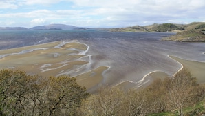 Un paisaje costero con una playa, árboles y colinas al fondo.