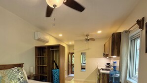 Quarto com cama, ventilador de teto e banheiro com chuveiro.