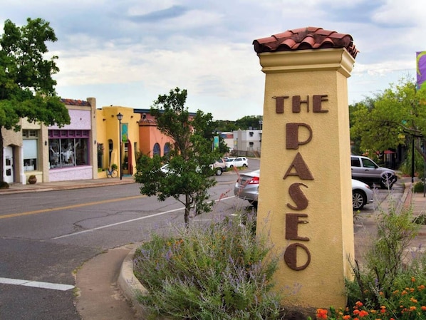 Un panneau de signalisation indiquant « THE DASEO », placé sur un pilier de couleur beige, entouré de verdure et de voitures garées.