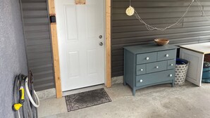 Une porte blanche avec un cadre en bois, une commode bleue avec des tiroirs, un petit bol en bois posé sur le dessus, et un sol en béton.