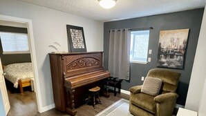 Un salon avec un piano, un fauteuil marron, un tapis et une affiche motivante accrochée au mur.