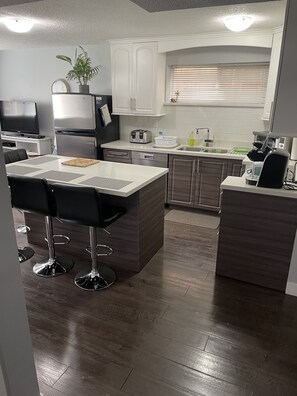 Una cocina moderna con armarios blancos, horno empotrado, microondas y pileta. Hay un comedor con mesa y sillas.