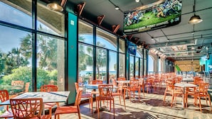 Un restaurante espacioso con amplias ventanas, sillas color naranja y vistas a palmeras.