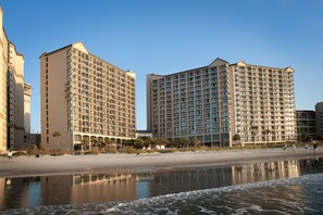 Un hôtel situé en bord de mer, composé de plusieurs immeubles de grande hauteur, avec une plage de sable et une mer calme.