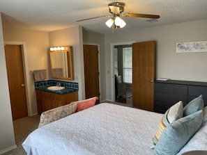 A bedroom with a bed, a vanity with a mirror, a ceiling fan, and a dresser.