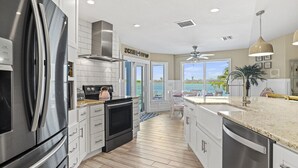 A modern kitchen with stainless steel appliances, white cabinetry, and a view of the ocean.