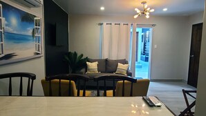 A modern living room with a dining table, sofa, and a large window with curtains.