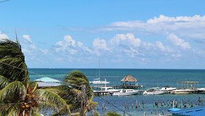 A marina with boats docked, a thatched-roof structure, and palm trees.