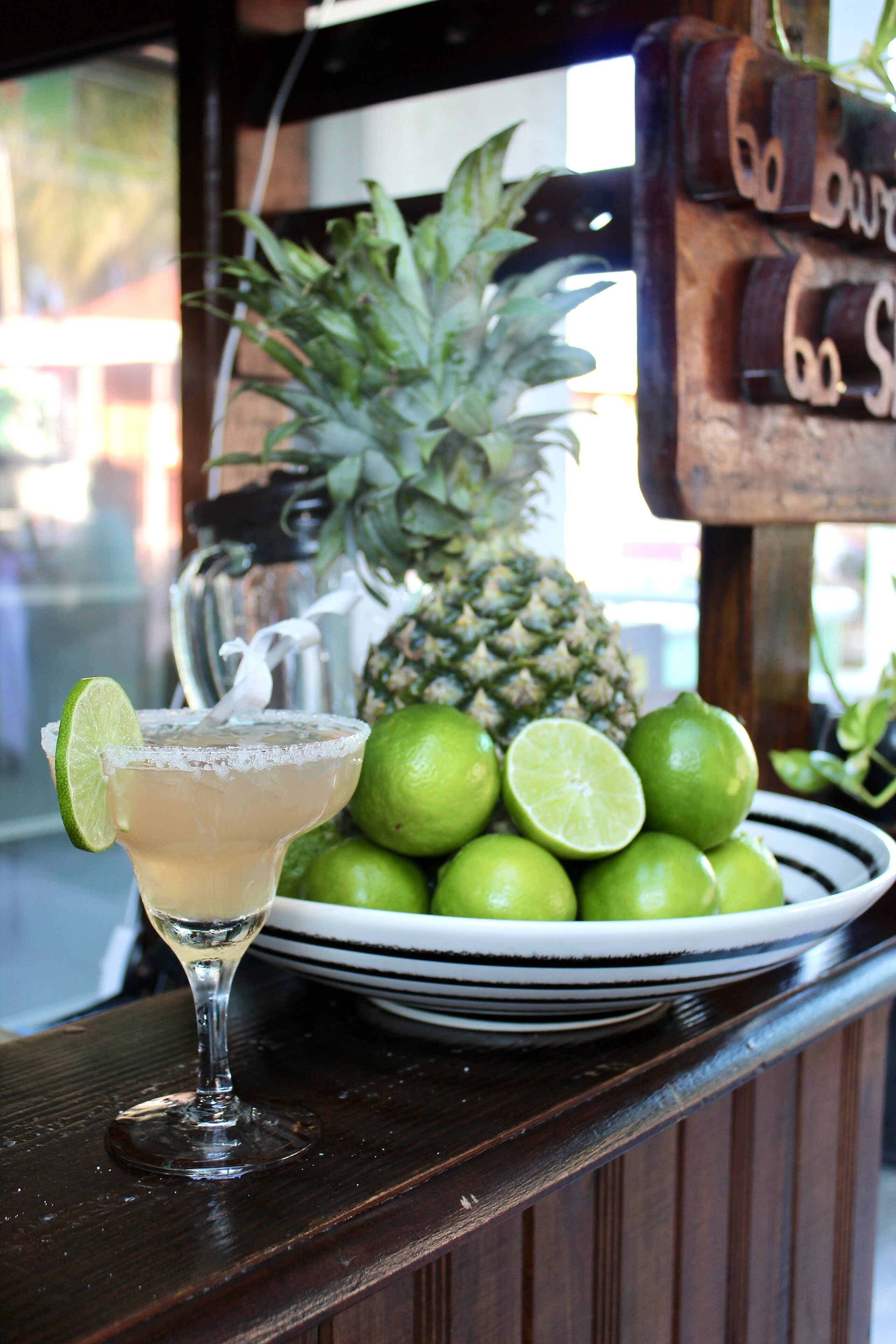 Un bar con un vaso de margarita, una piña y limones sobre una encimera de madera.