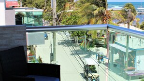 A balcony with wicker furniture, a view of a street with palm trees, and a clear sky.