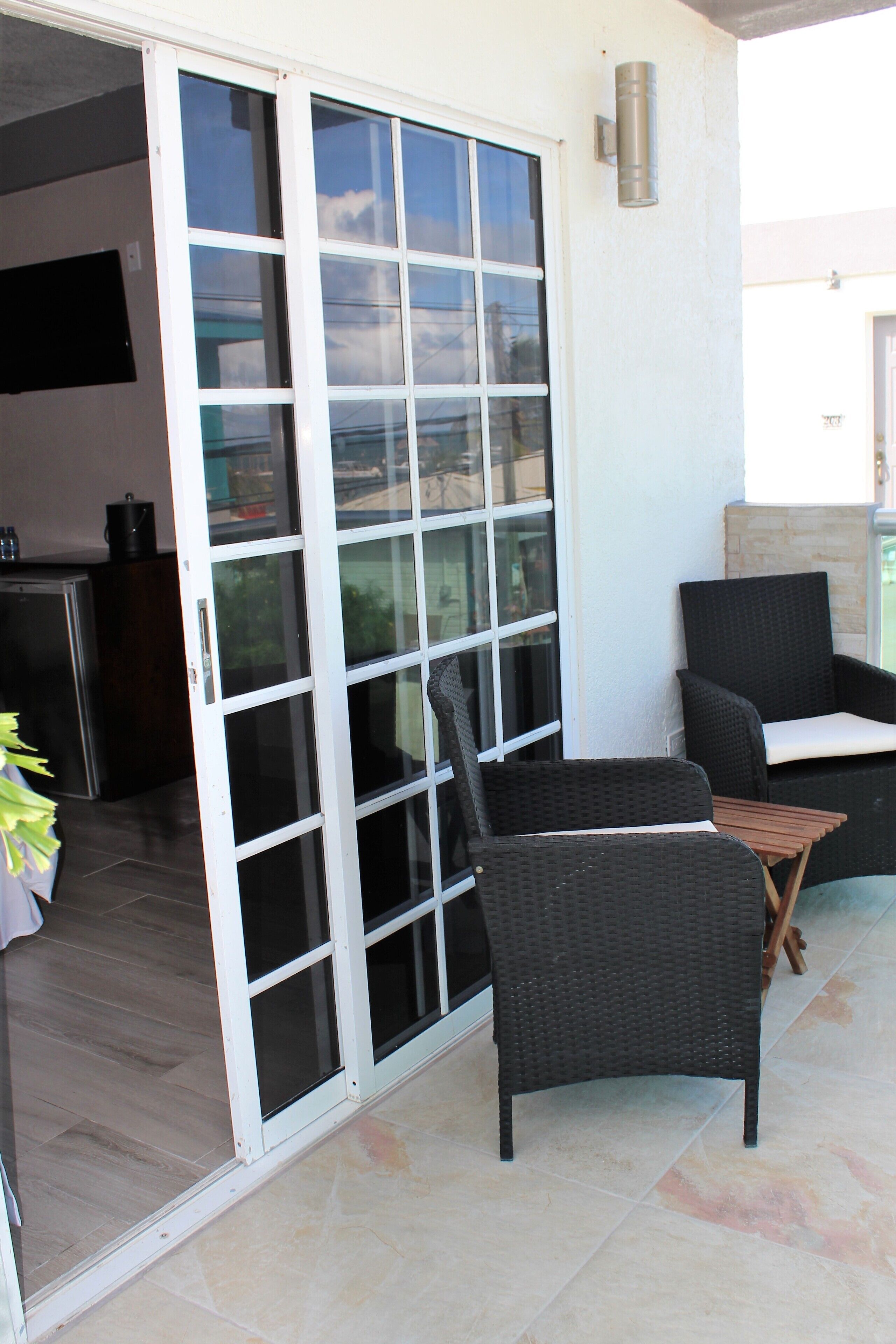 Een patio met een schuifdeur naar een keuken, twee rieten stoelen en een bijzettafeltje.