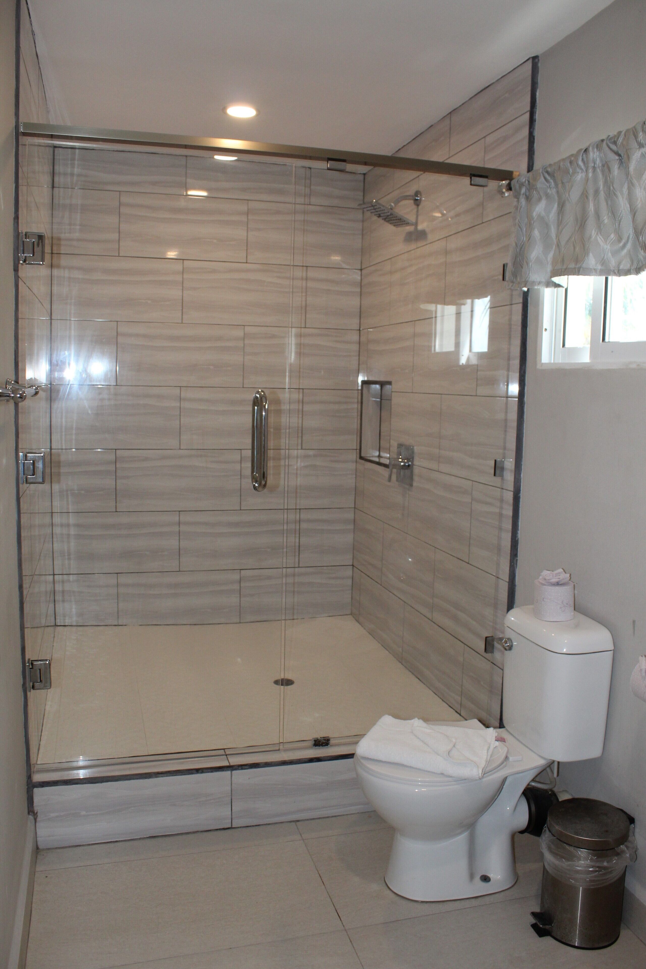 Un baño moderno con ducha envuelta en vidrio, inodoro y un cubo de basura.