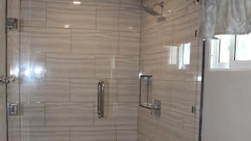 Un baño moderno con ducha envuelta en vidrio, inodoro y un cubo de basura.