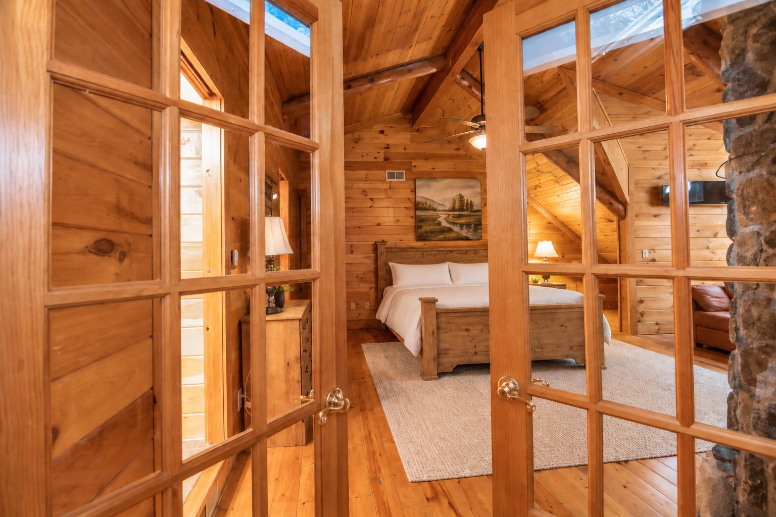 A wooden cabin interior with a bed, a painting, and a stone pillar.