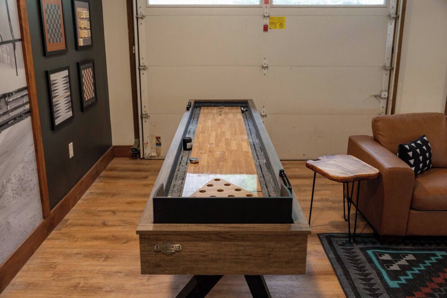 A room with a shuffleboard table, a brown leather couch, and a small wooden table with a cushion.