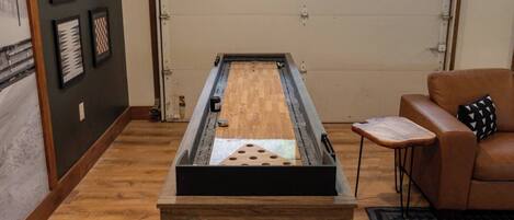 A room with a shuffleboard table, a brown leather couch, and a small wooden table with a cushion.