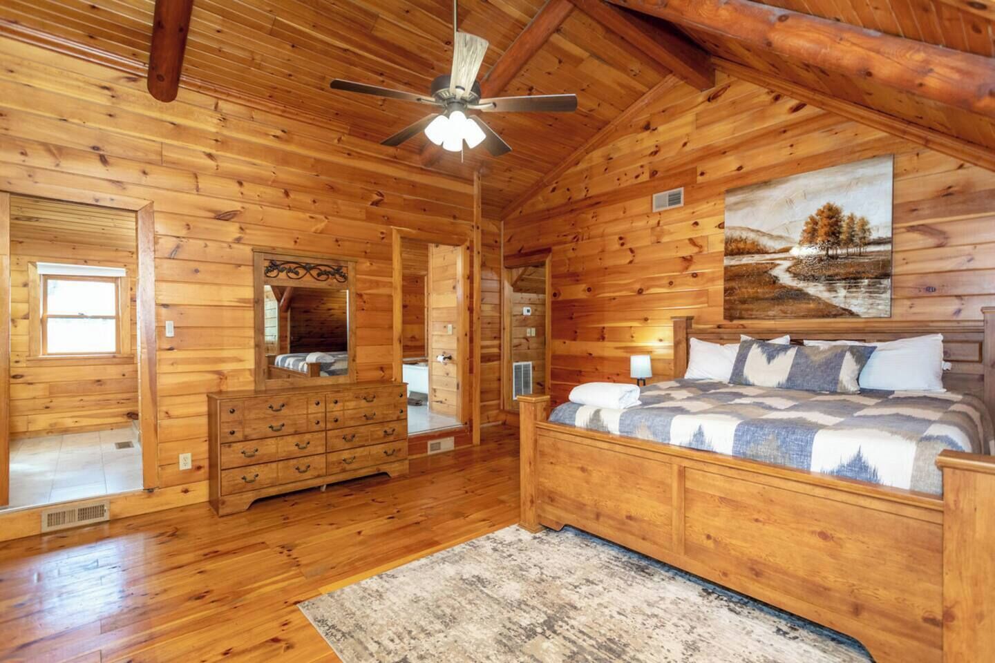 A wooden cabin bedroom with a bed, dresser, and a ceiling fan.
