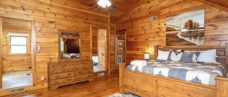 A wooden cabin bedroom with a bed, dresser, and a ceiling fan.