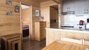 A wooden interior with a kitchen area featuring a stove, sink, and cabinets. There is a wooden bench and a small table.
