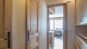 A wooden hallway with a door leading to a room with a window, a radiator, and a chair.