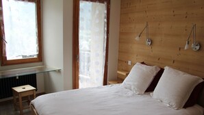 A bedroom with a large bed, wooden headboard, two bedside lamps, a small wooden stool, and a glass shelf. - Renovated 2-bedroom apartment, station center, WIFI (La Clusaz)
