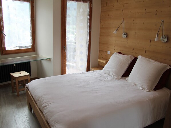 A bedroom with a large bed, wooden headboard, two bedside lamps, a small wooden stool, and a glass shelf.