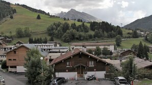 A mountain village with traditional wooden houses, a parking area, and a view of the surrounding hills. - Renovated 2-bedroom apartment, station center, WIFI (La Clusaz)