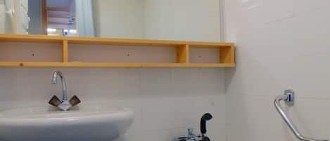 A bathroom with a white sink, a bathtub, and a shower. There is a wooden shelf above the sink and a handrail on the wall next to the bathtub.