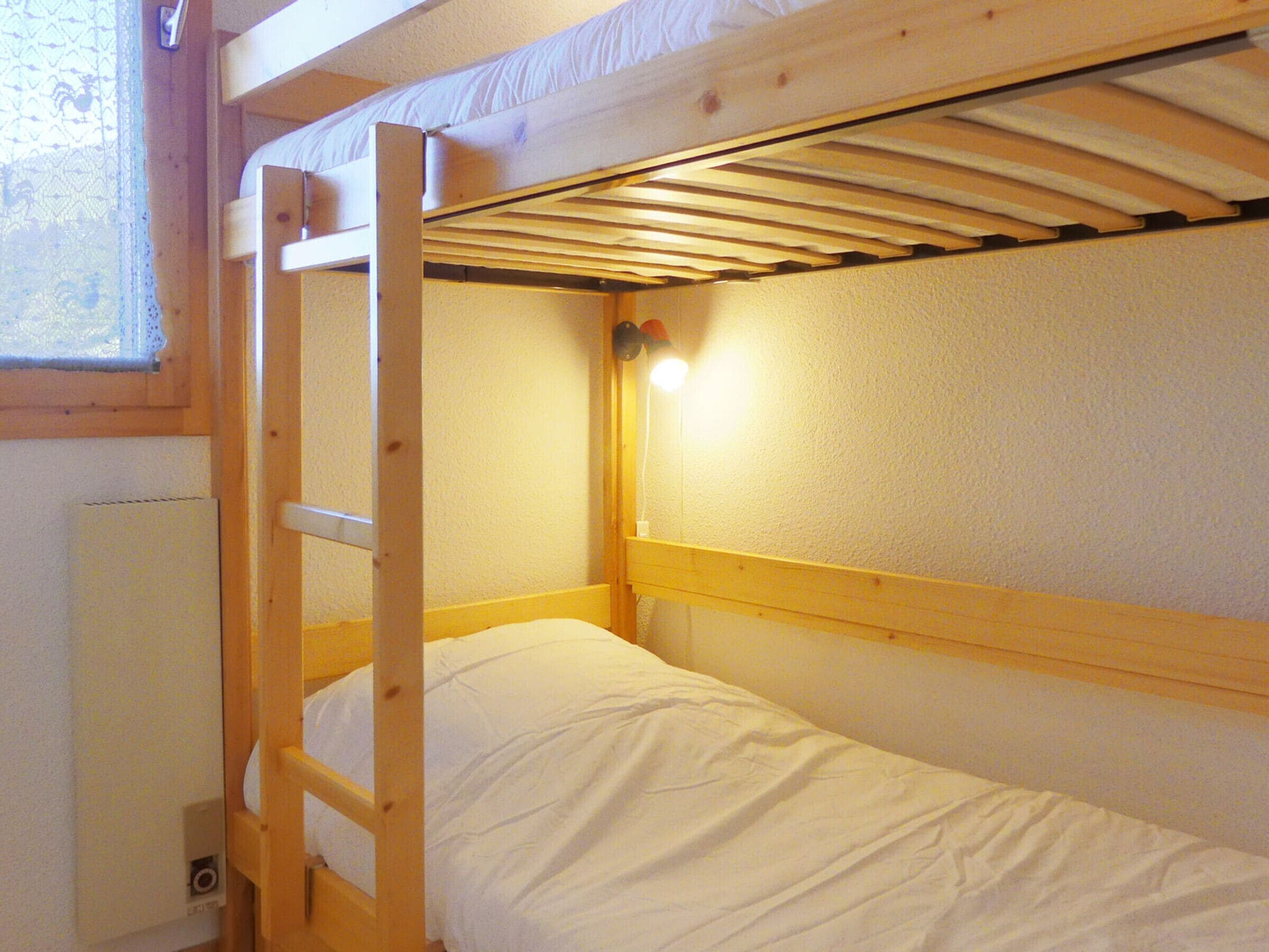A bunk bed with a ladder, white bedding, and a small window with a curtain.