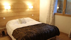 Ein Zimmer mit Holzwänden, einem Bett, zwei Wandleuchten und einem Fenster mit Vorhängen.