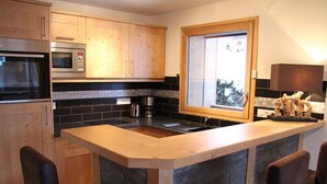 Eine moderne Küche mit Holzausstattung, einer integrierten Mikrowelle, einer Kaffeemaschine und einem großen Fenster.