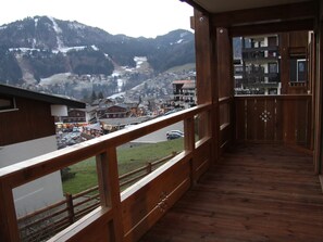 A wooden balcony with a view of a mountain town and a road. - Charming 2BR with hotel services and garage - La Clusaz (La Clusaz)