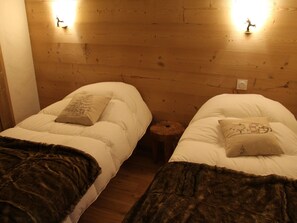 Deux lits simples avec des têtes de lit adossées à un mur en bois, une petite table ronde et une prise électrique murale.