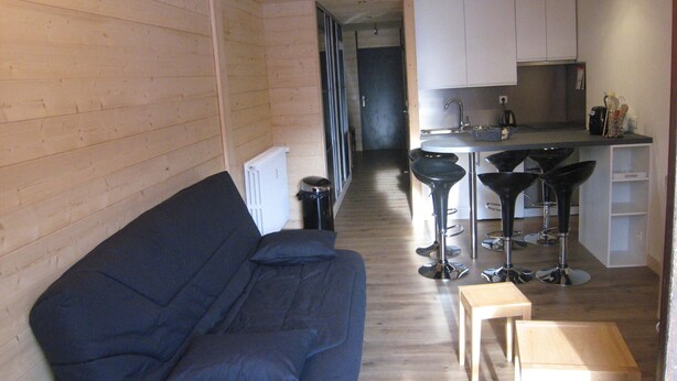 A compact living space with a sofa, a small table, and a kitchen area with a bar stool. - 2-Room Apartment, Ski-In/Ski-Out, South Balcony, Comfort for 6 (La Clusaz)