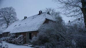 Lumipeitteinen talo, jossa on kalteva katto, tiiliverhous ja selvästi näkyvä savupiippu.