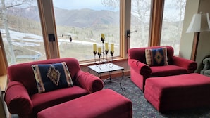 A room with two red sofas, a small table with candles, and a view of mountains through large windows.