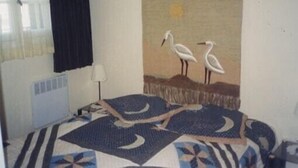 Een kamer met een bed met een geborduurde spreideken, een wanddecoratie van twee vogels, een raam met gordijnen en een radiator.